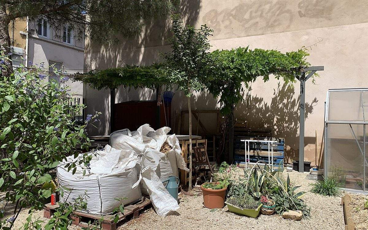 Coin d'un jardin partagé urbain à Lyon, avec pergola, arrosoir, serre et sacs de compost